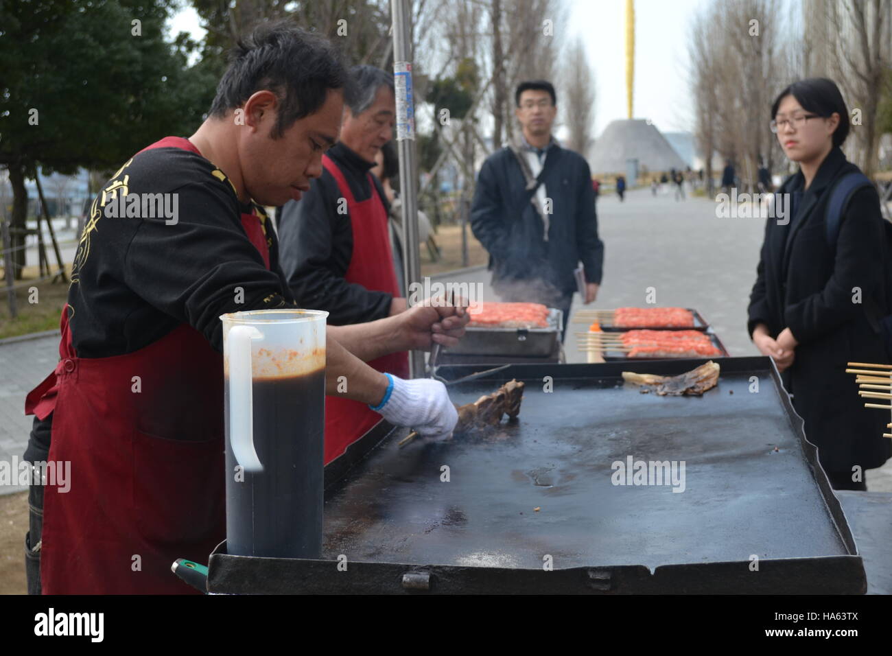 Tokyo, Japan-2/26/16: Two street food vendors grilling yakitori chicken on a portable flat skillet grill while two customers wait for their order. Stock Photo