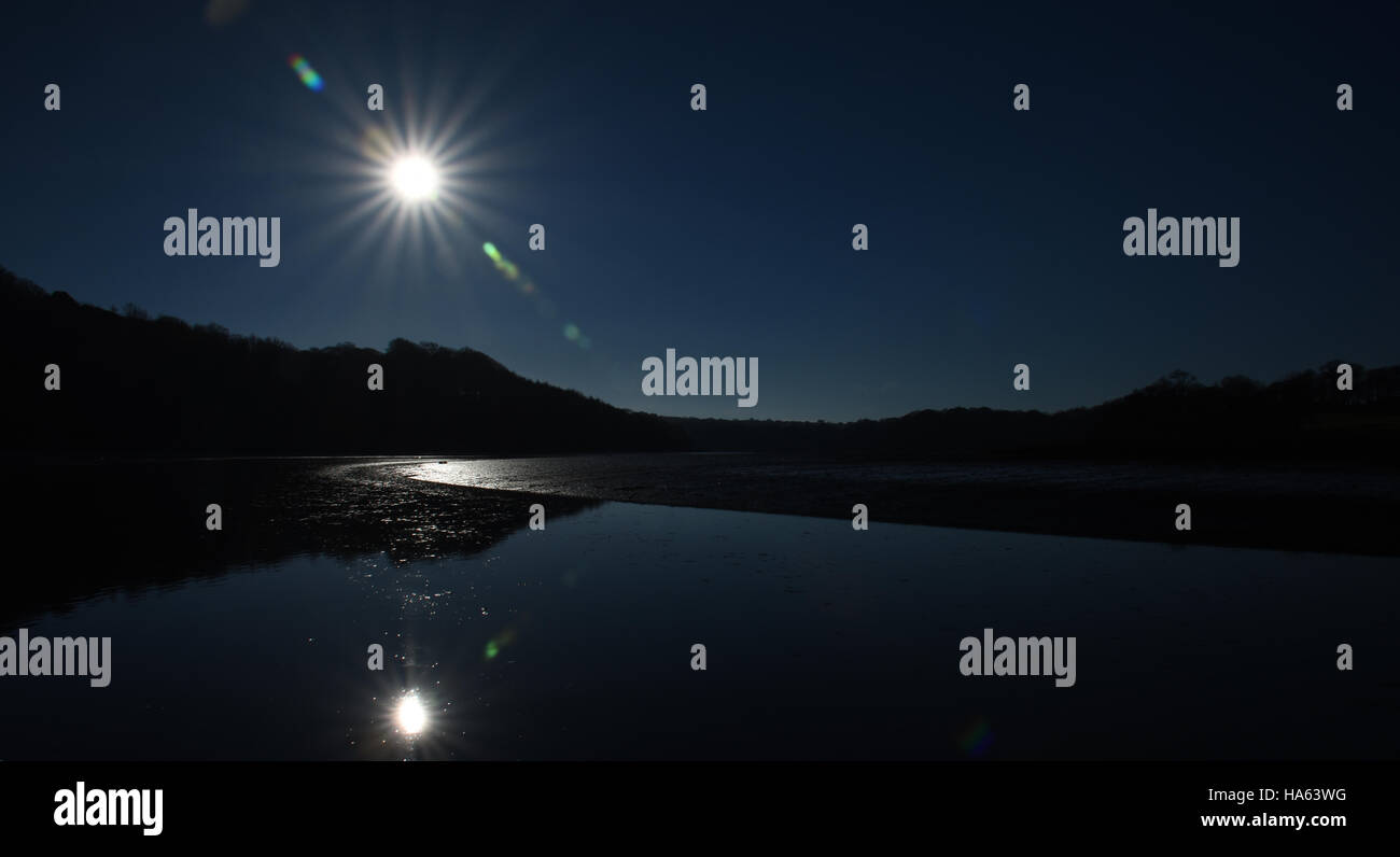 Starry sun reflects in calm water at low tide making a silhouette with deep blue sky Stock Photo