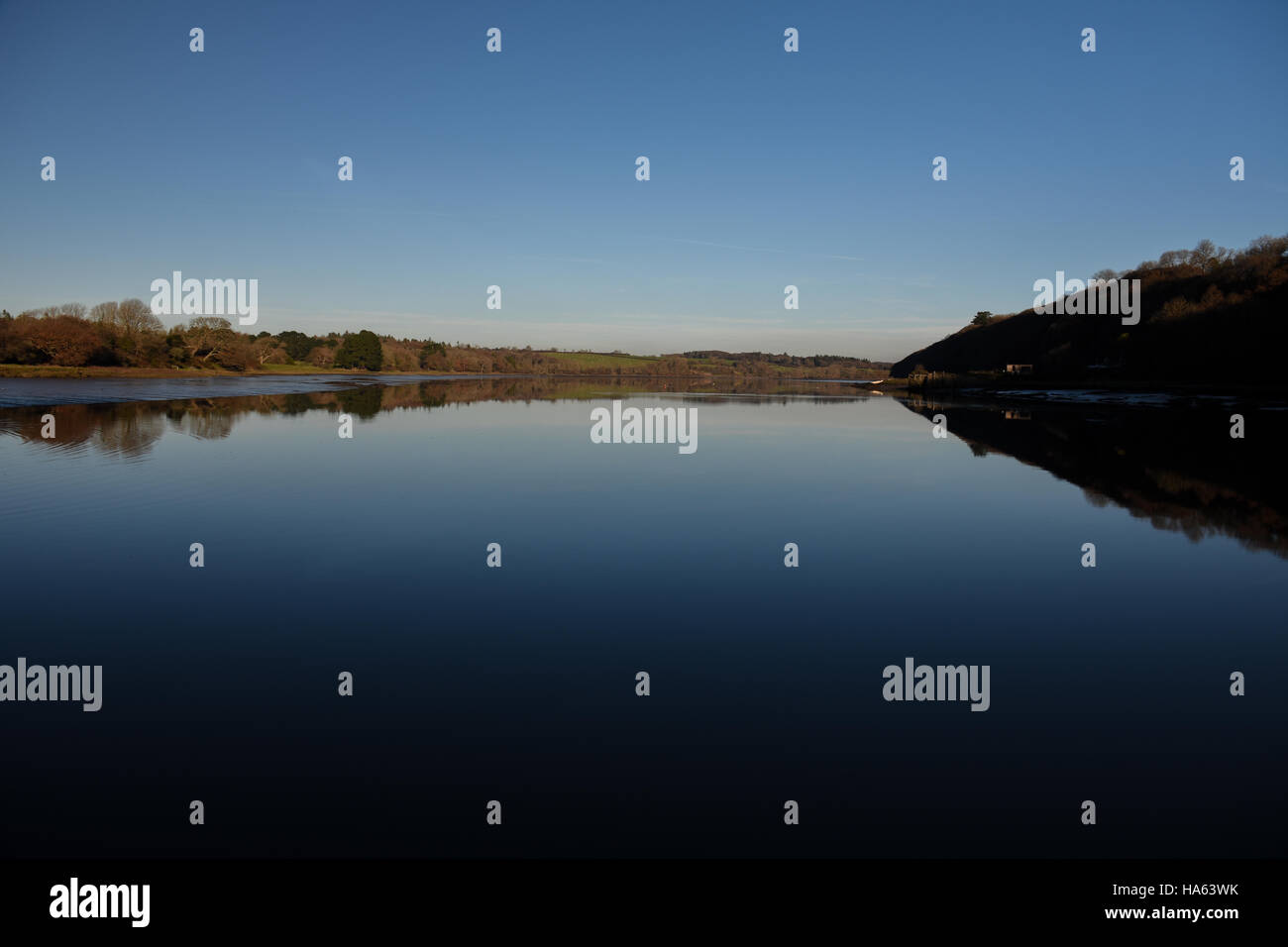 Blue sky and river bank reflected in perfectly calm water Stock Photo ...