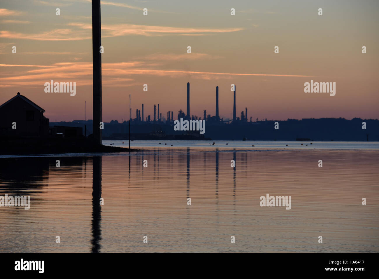 Pembroke refinery silhouetted in a sunset. Reflected in calm water with orange clouds and blue sky Stock Photo