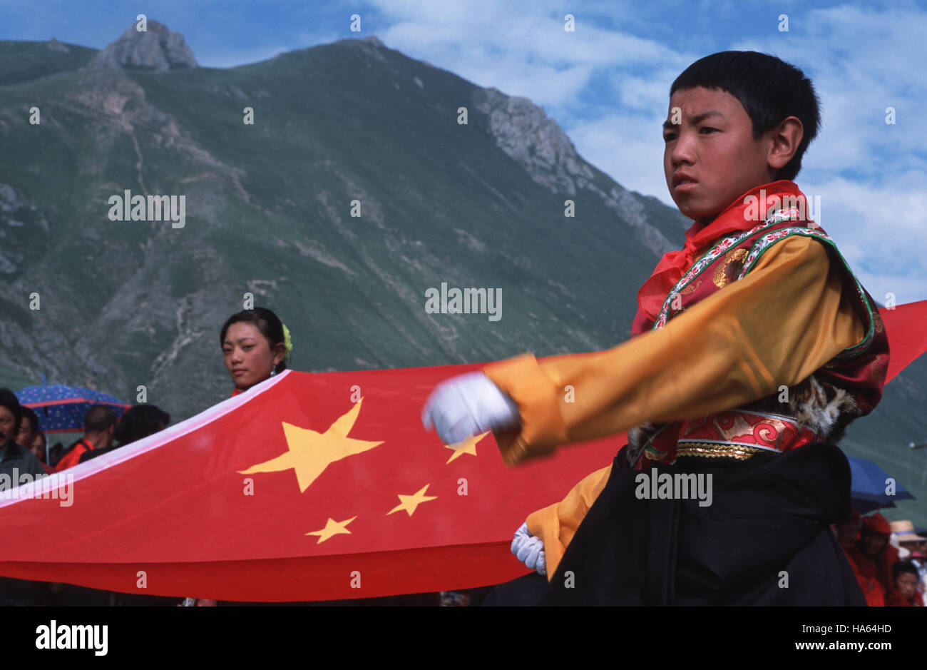 Caption: Yushu, Sichuan, China - Aug 2002. A young ethnic Tibetan boy carrying the Chinese flag while striding to music reciting 'make China stronger' Stock Photo