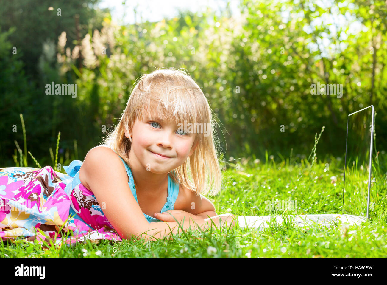 Little girl laying with laptop in a summer garden Stock Photo