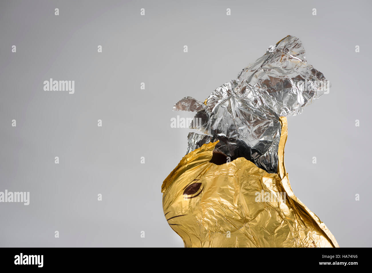 Chocolate Easter bunny, wrapped in shiny golden and silver aluminum foil, partially nibbled away, foil ripped open at the top Stock Photo