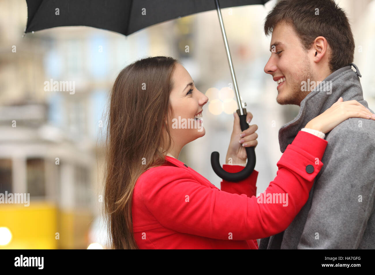 Side view of a couple encounter in the street under an umbrella in a rainy day Stock Photo