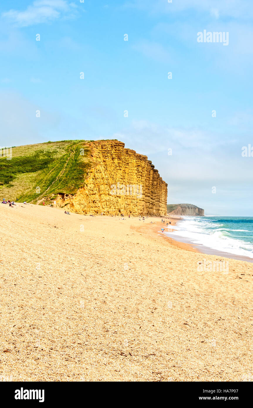 A steep path climbs from relatively flat sand through green vegetation to the top of the vertical East Cliff at Bridport Sands Stock Photo