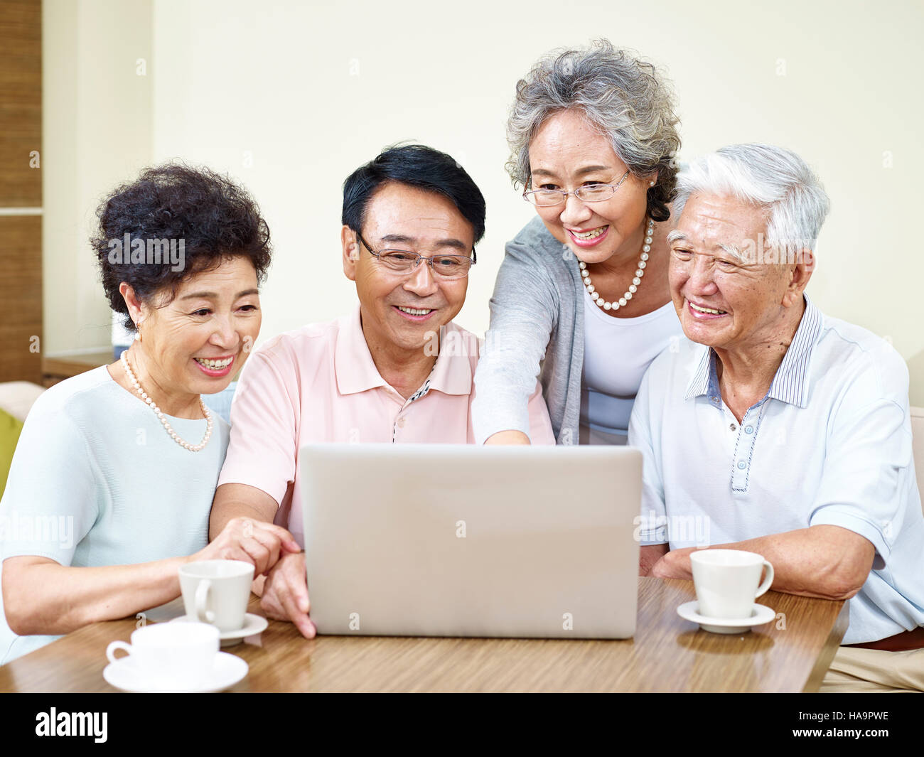four senior asian people gathering at home using laptop computer together. Stock Photo