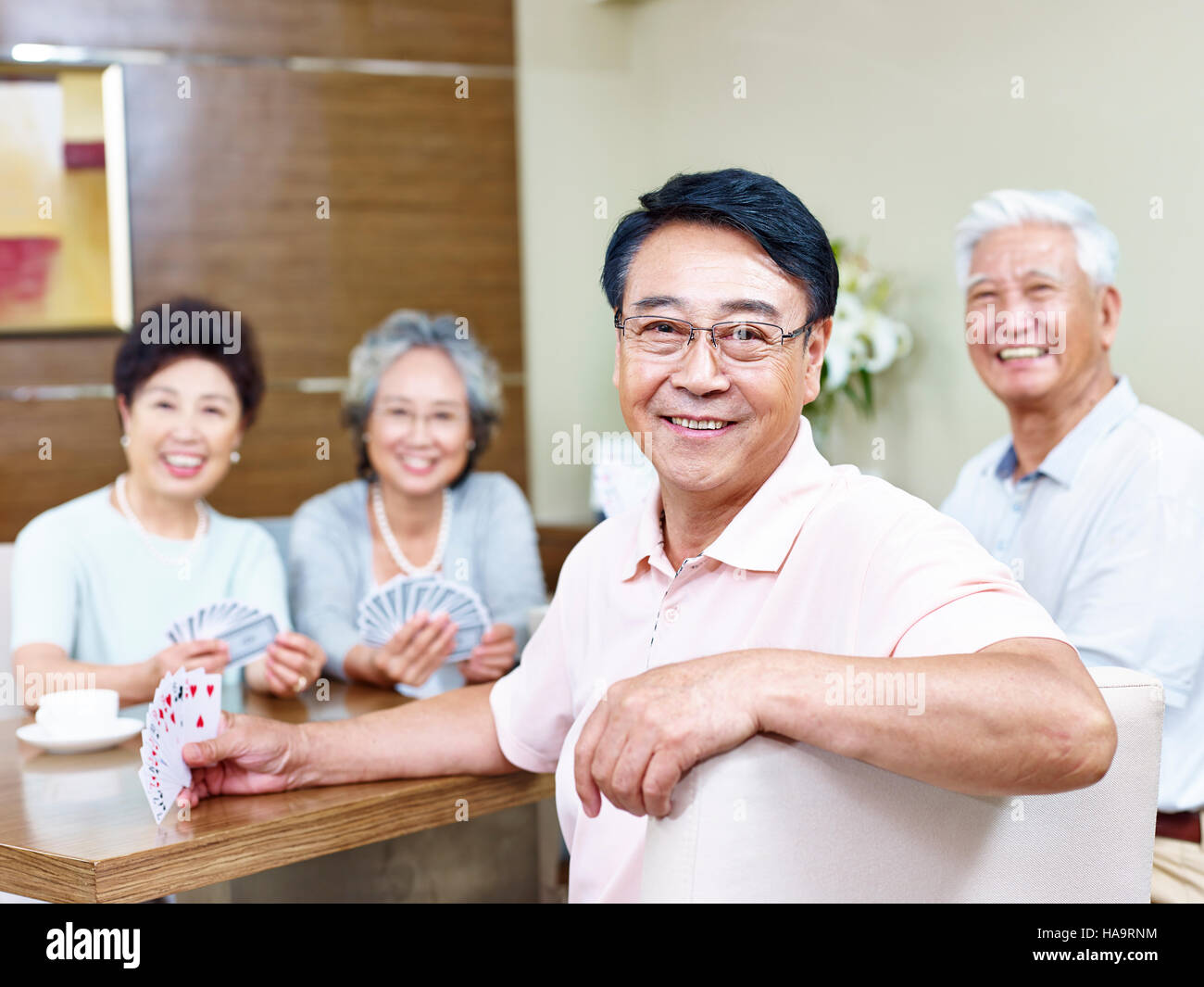 senior asian man looking at camera smiling while playing cards with friends. Stock Photo
