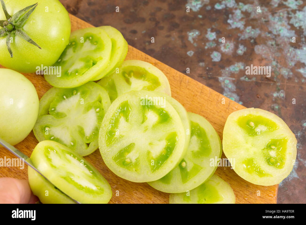 hand slicing green tomatoes on a wooden cutting board Stock Photo