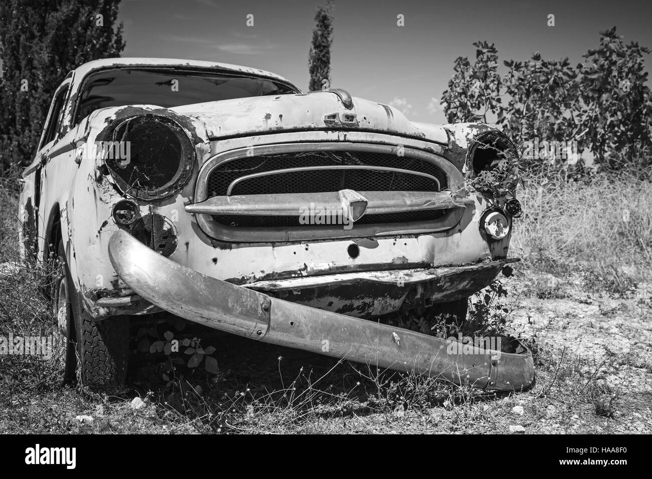 Zakynthos, Greece - August 20, 2016: Old abandoned rusted car stands in summer garden, closeup monochrome photo Stock Photo