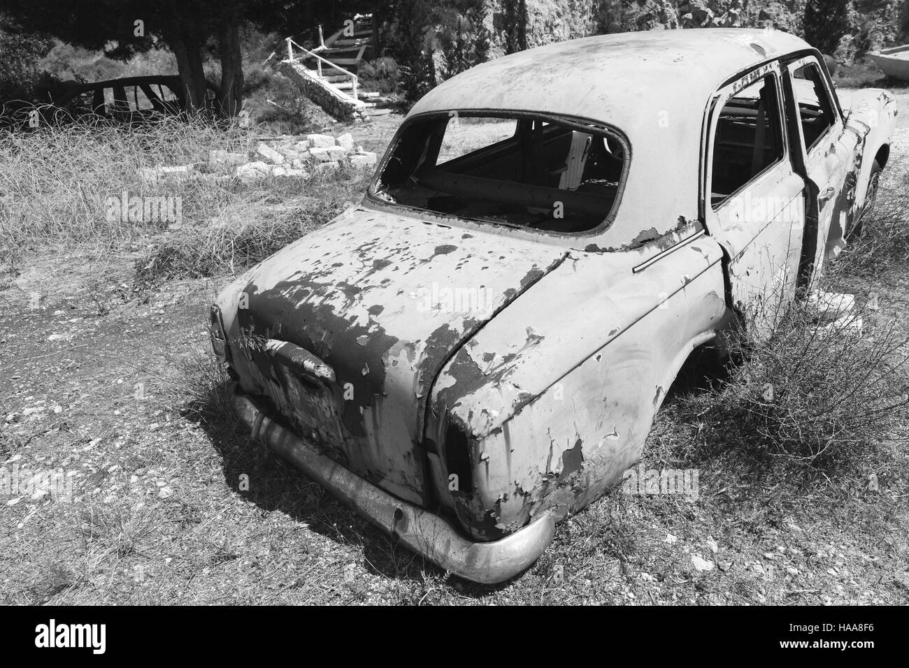 Zakynthos, Greece - August 20, 2016: Old abandoned rusted car stands in summer garden, rear view, black and white Stock Photo