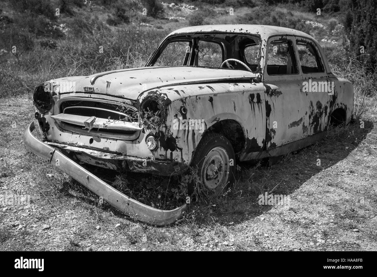 Zakynthos, Greece - August 20, 2016: Old abandoned rusted car stands in summer garden, black and white Stock Photo