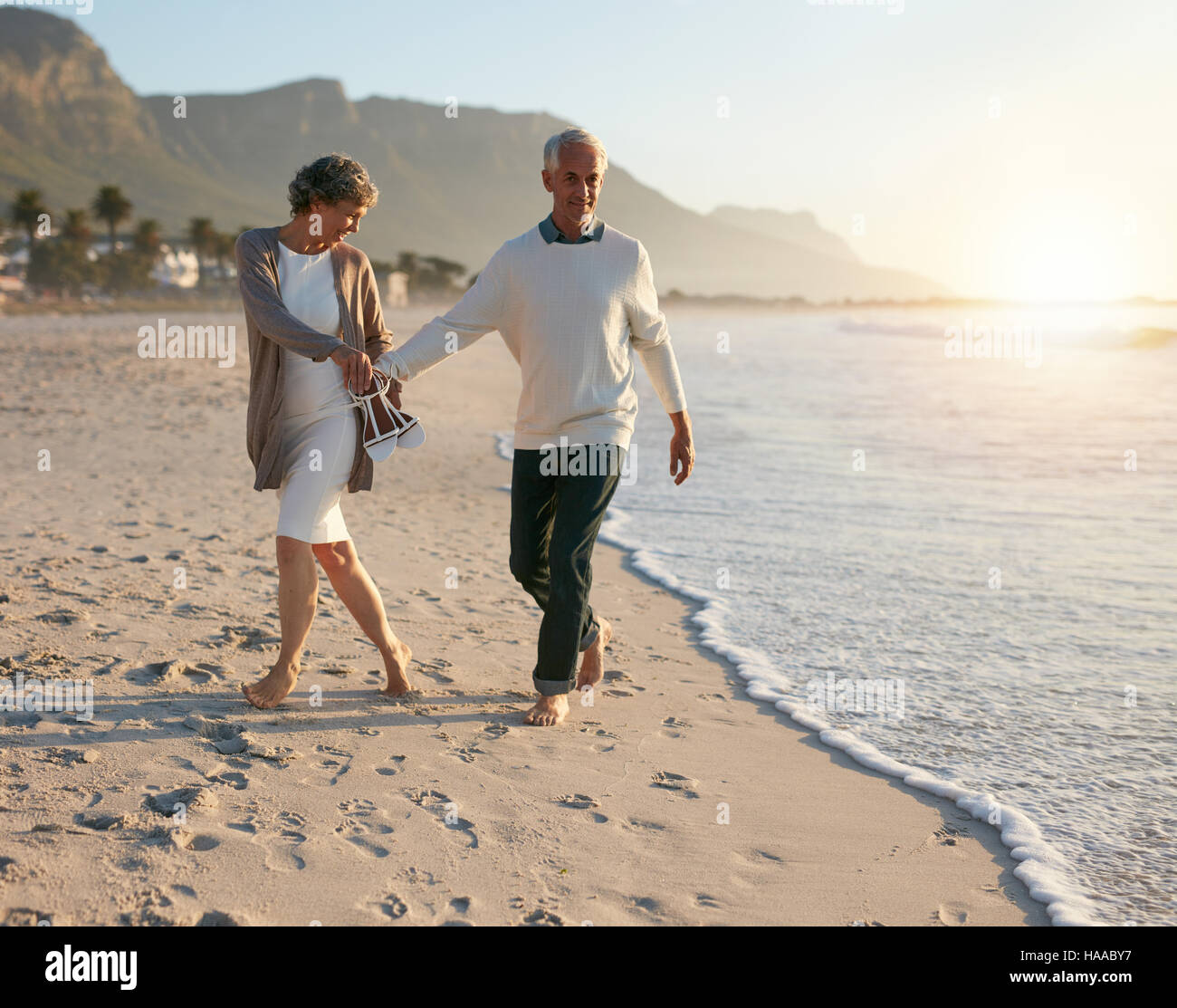 Senior couple walking leisurely on the beach while holding hands ...