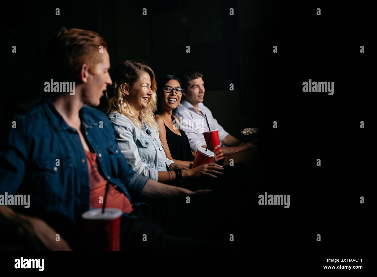 Group of friends sitting in multiplex movie theater and watching movie. Happy young people watching movie in cinema. Stock Photo