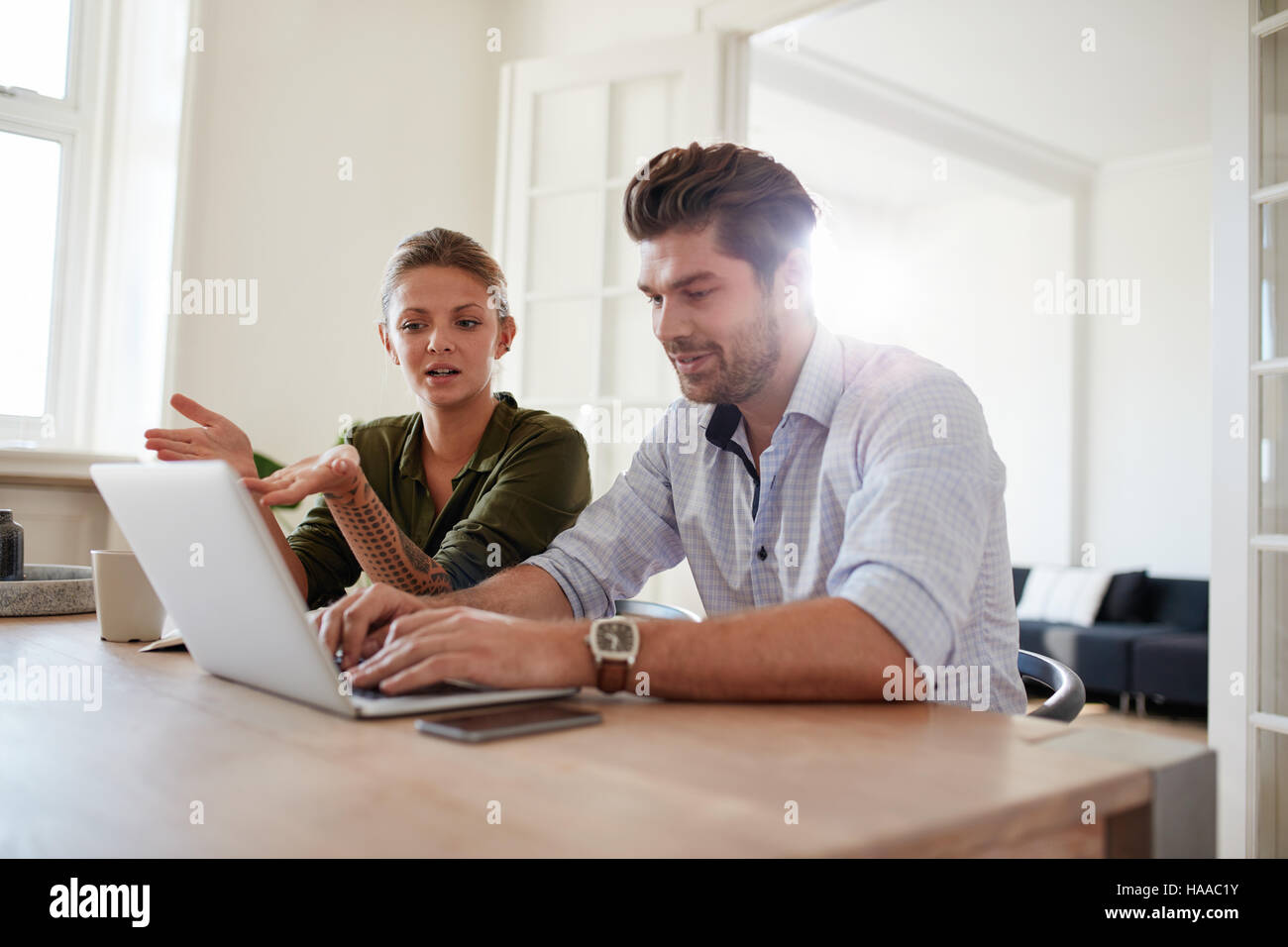 Shot of young couple sitting together at table and working on laptop. Young man and woman at home using laptop. Stock Photo