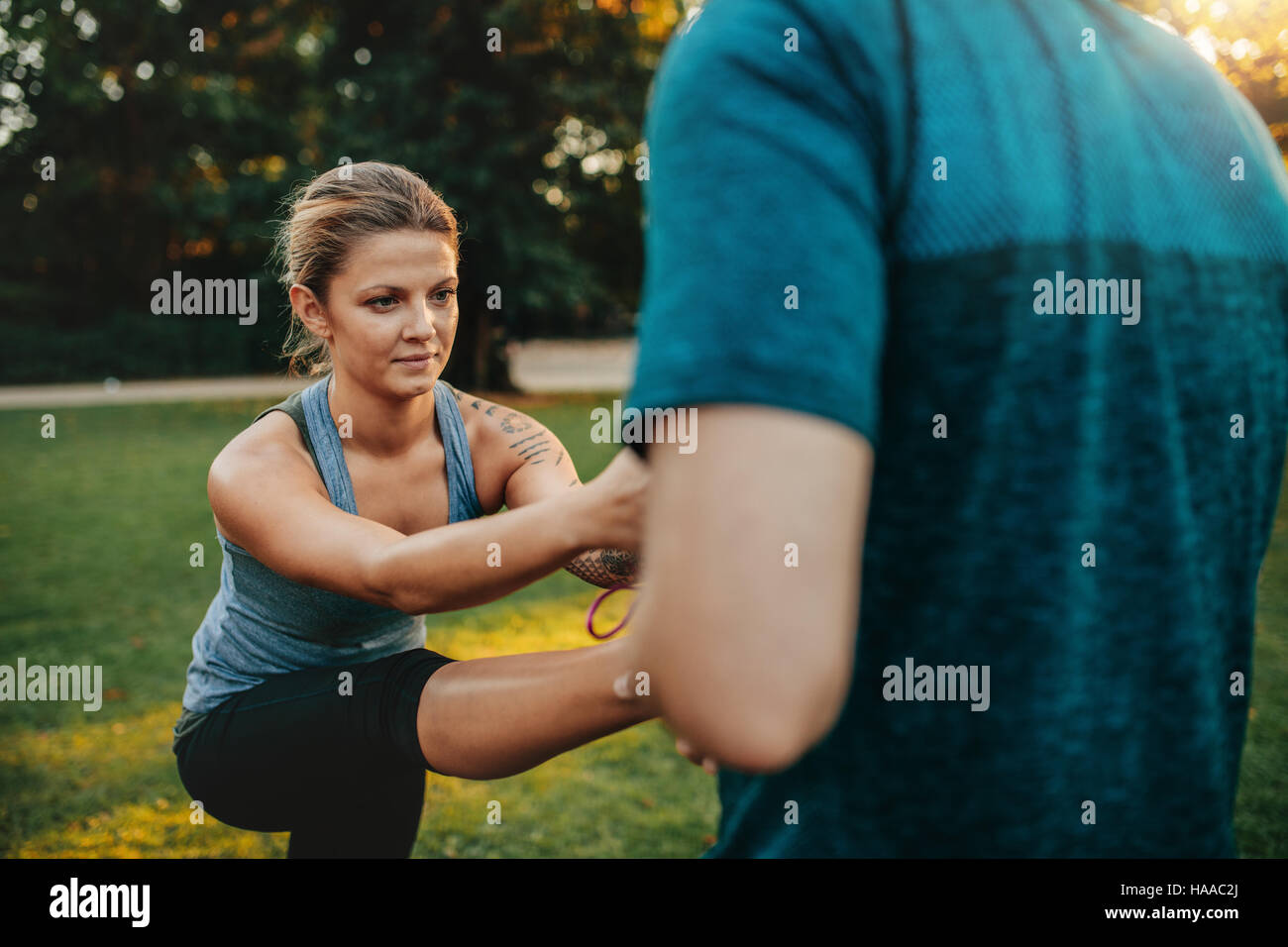 Young woman being assisted by personal trainer in stretching exercises at park. fitness female working out with help from coach. Stock Photo