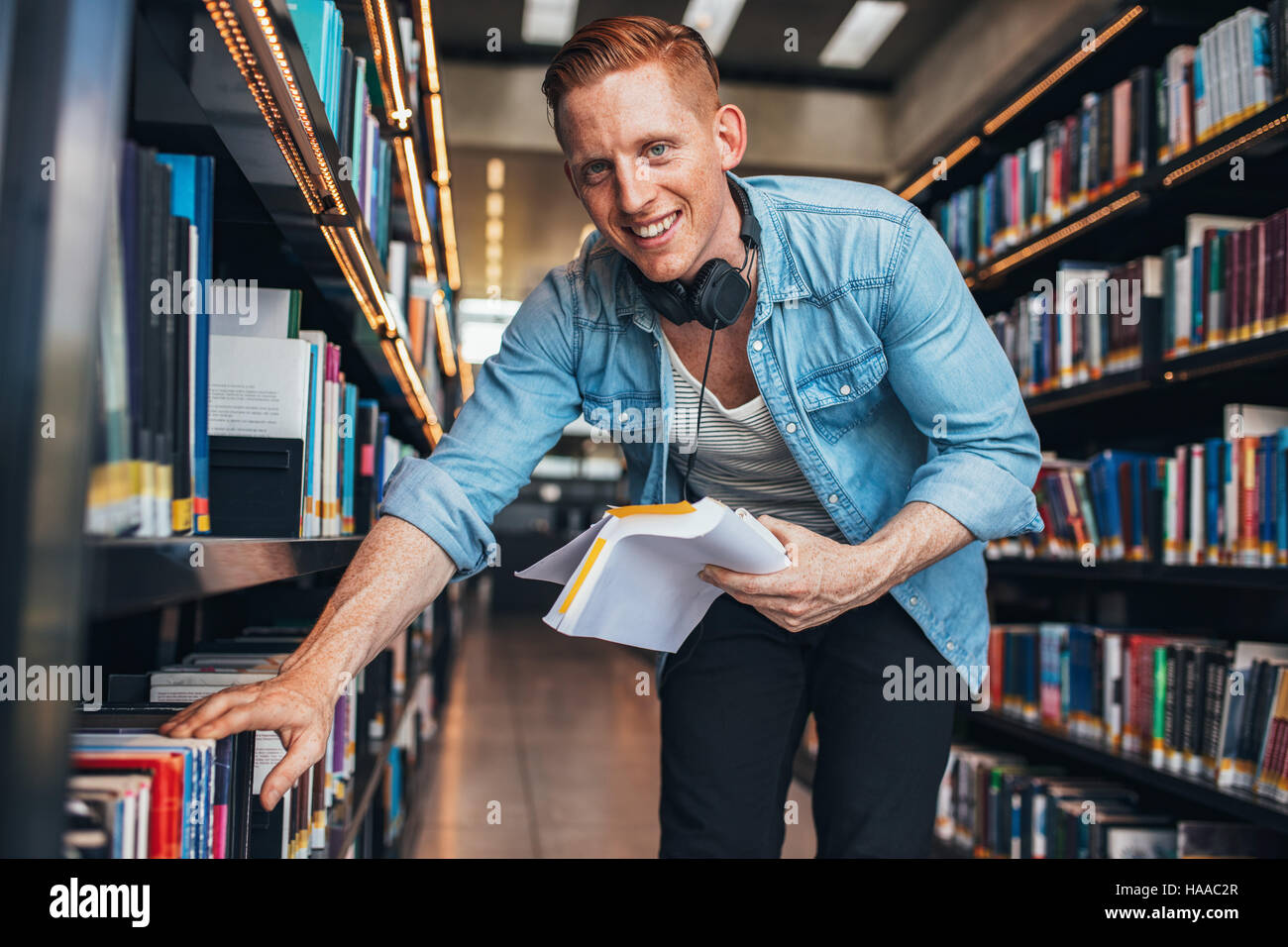 Young caucasian man finding books in public library. Finding information for his studies. Stock Photo