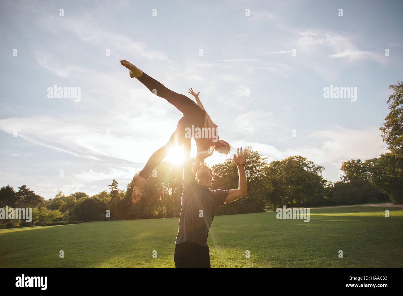 Healthy young man and woman doing various yoga poses in pair outdoors. Fit couple doing acroyoga in park. Stock Photo