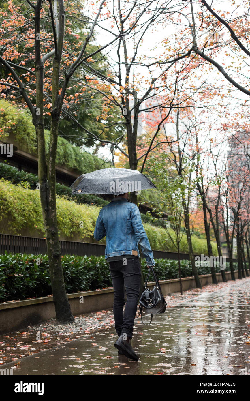 Man with handbag and umbrella walking on pedestrian walkway Stock Photo ...