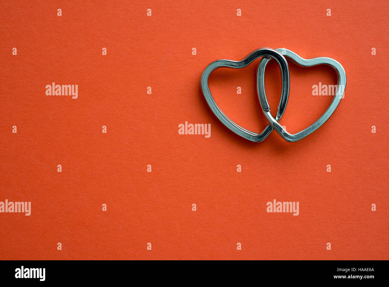 two linked metallic hearts on red background Stock Photo