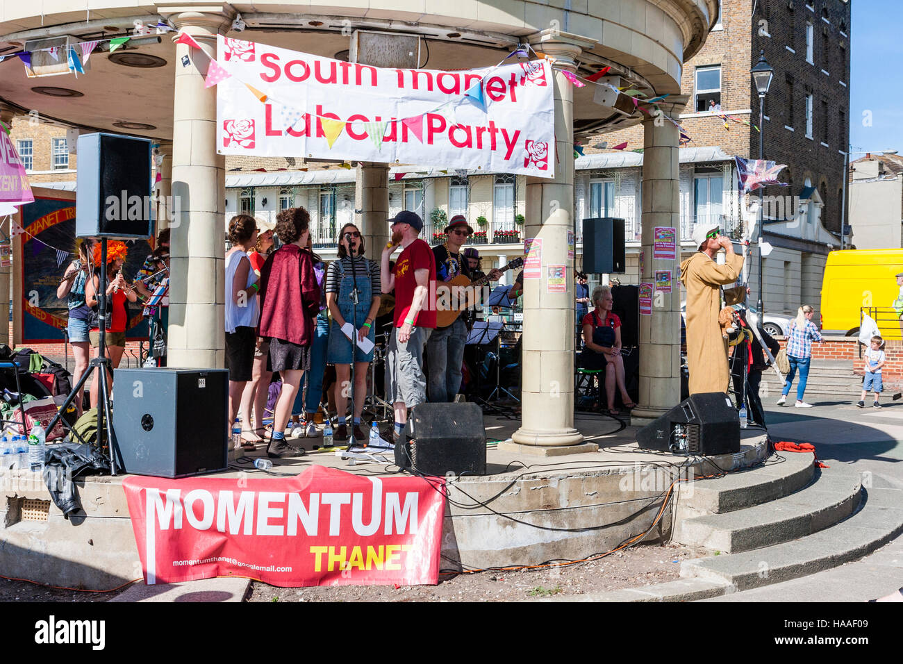 England, Ramsgate. Jeremy Corbyn Momentum rally. Male singer perfomes outdoors on bandstand with backing singers and group. Political banners. Stock Photo