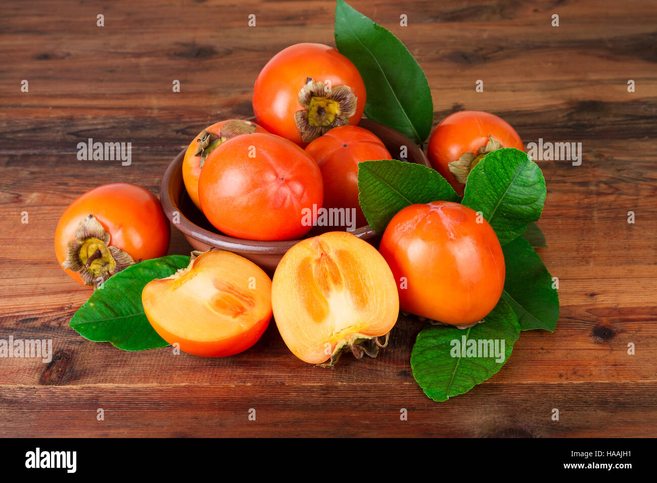 Persimmons with green leaves on old wooden background Stock Photo