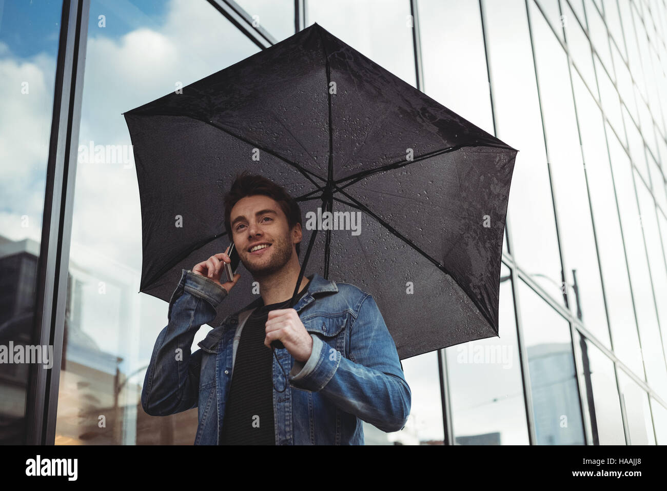 Man holding umbrella and talking on mobile phone Stock Photo