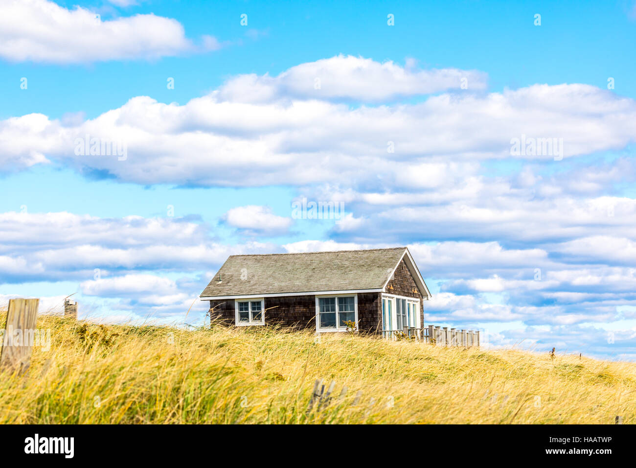 small house in a grassy area with blue sky and puffy white clouds Stock Photo