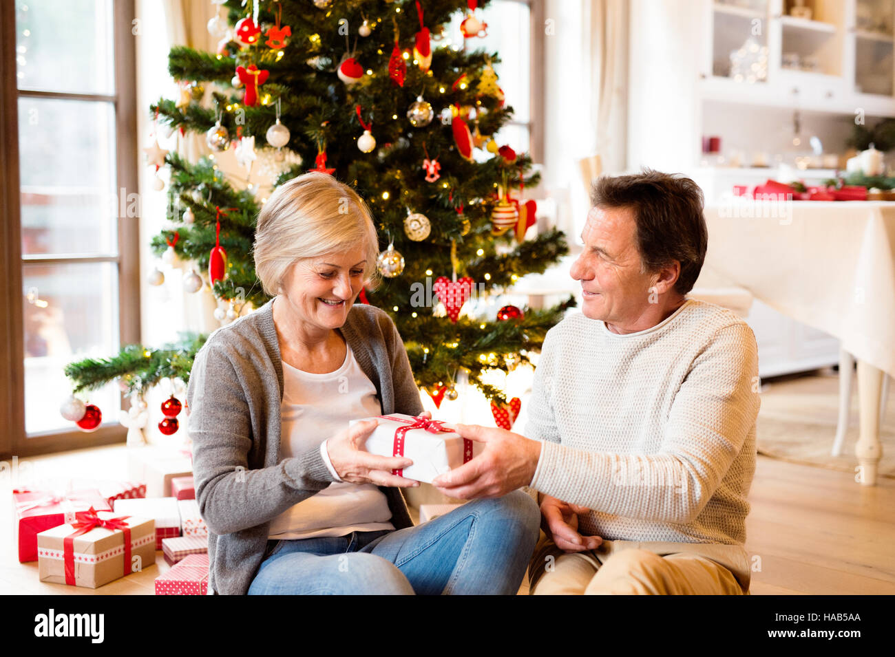 Senior couple in front of Christmas tree with presents. Stock Photo