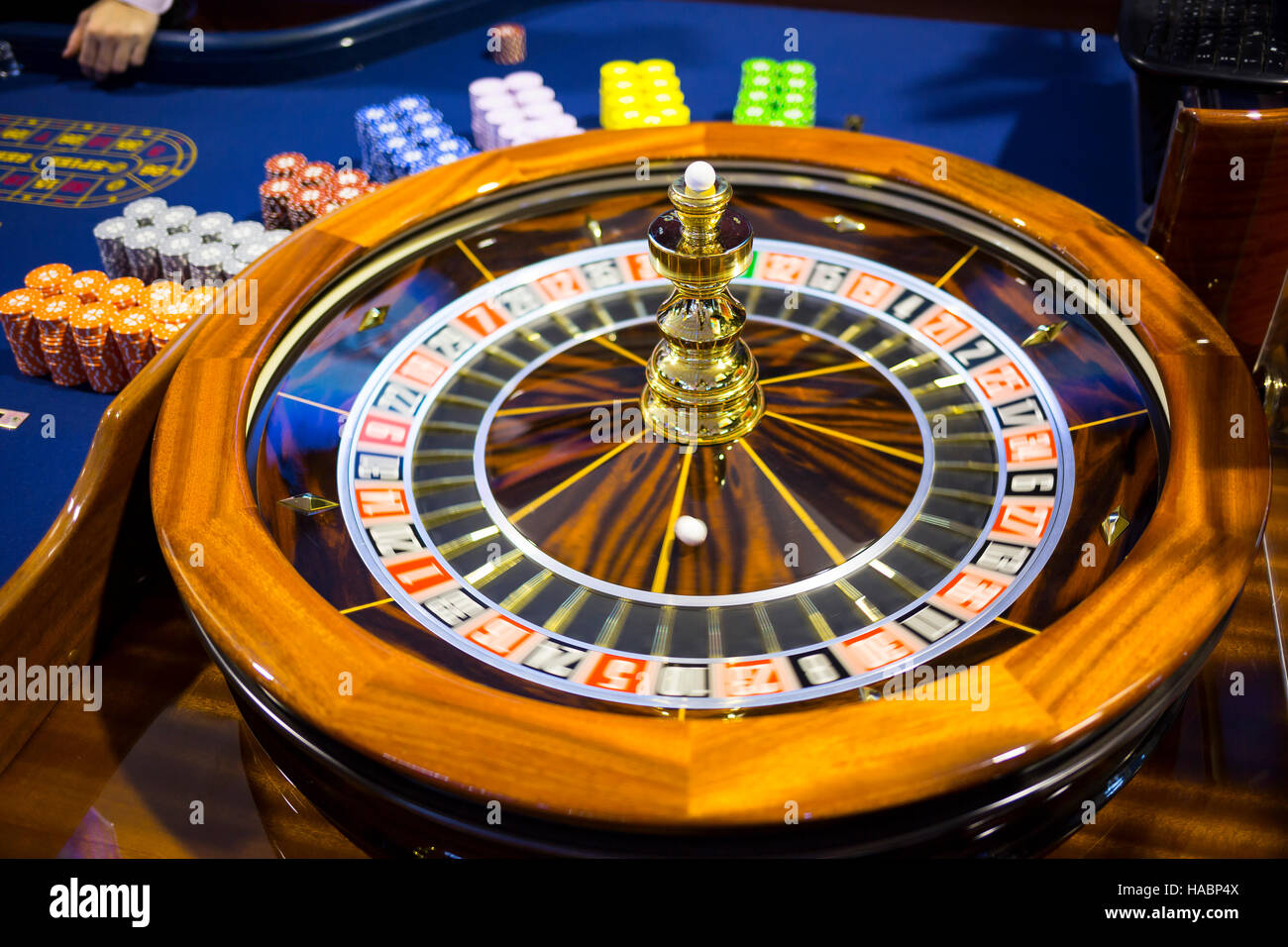 Wooden colourful casino roulette. Casino machine and gambling equipment. Roulette table with chips next to the roulette. Spinning roulette in motion. Stock Photo