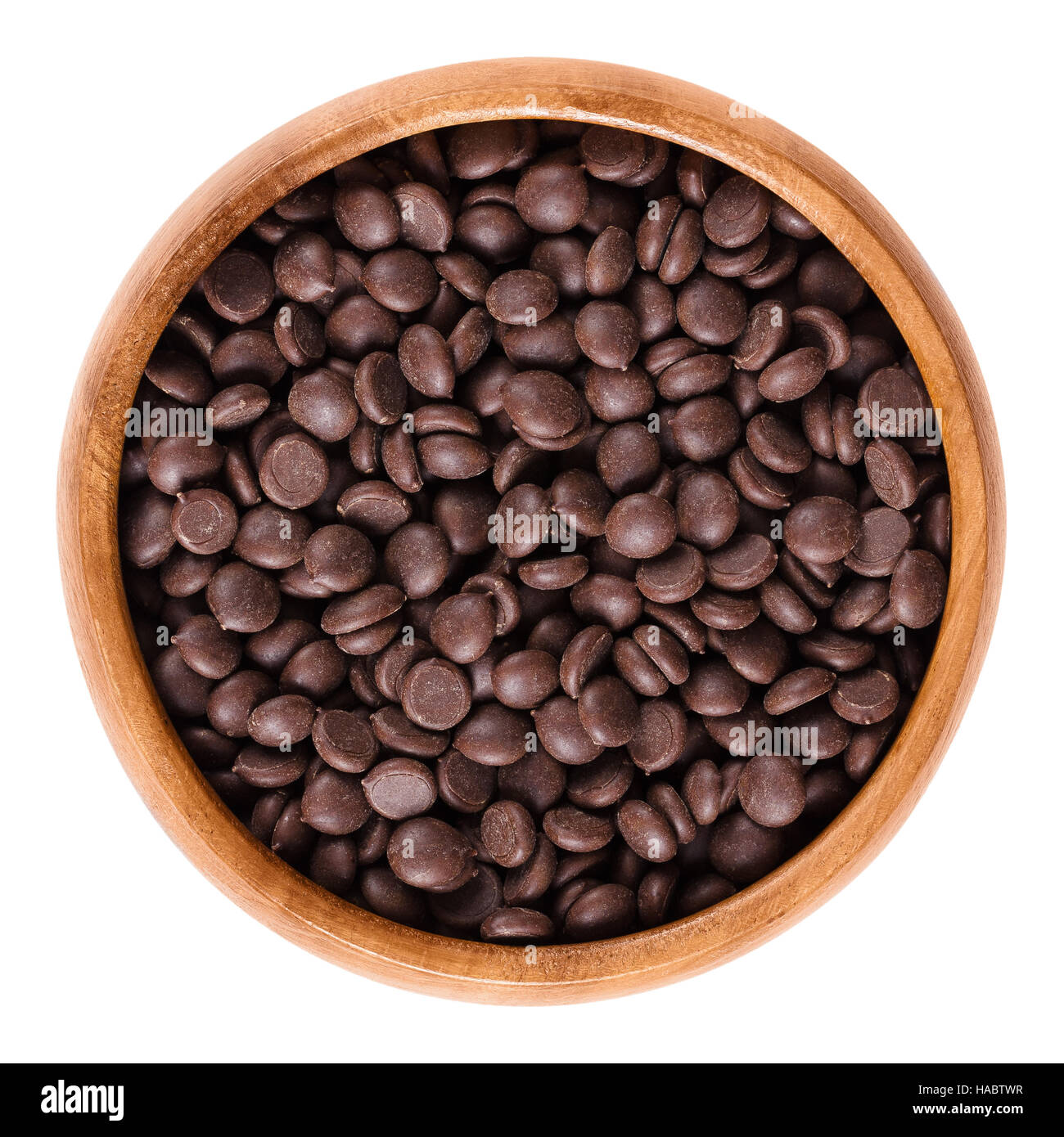 Dark chocolate drops in wooden bowl, ingredient used for cookies and muffins. Edible brown cocoa product. Isolated macro photo. Stock Photo