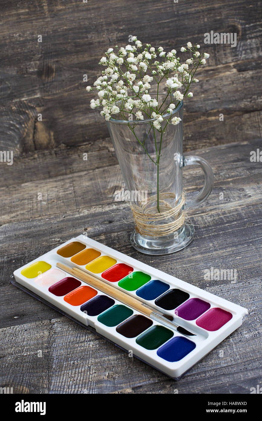 Sprig of gypsophilas in vase and watercolor paints on grey wooden background. Vertical imagination Stock Photo