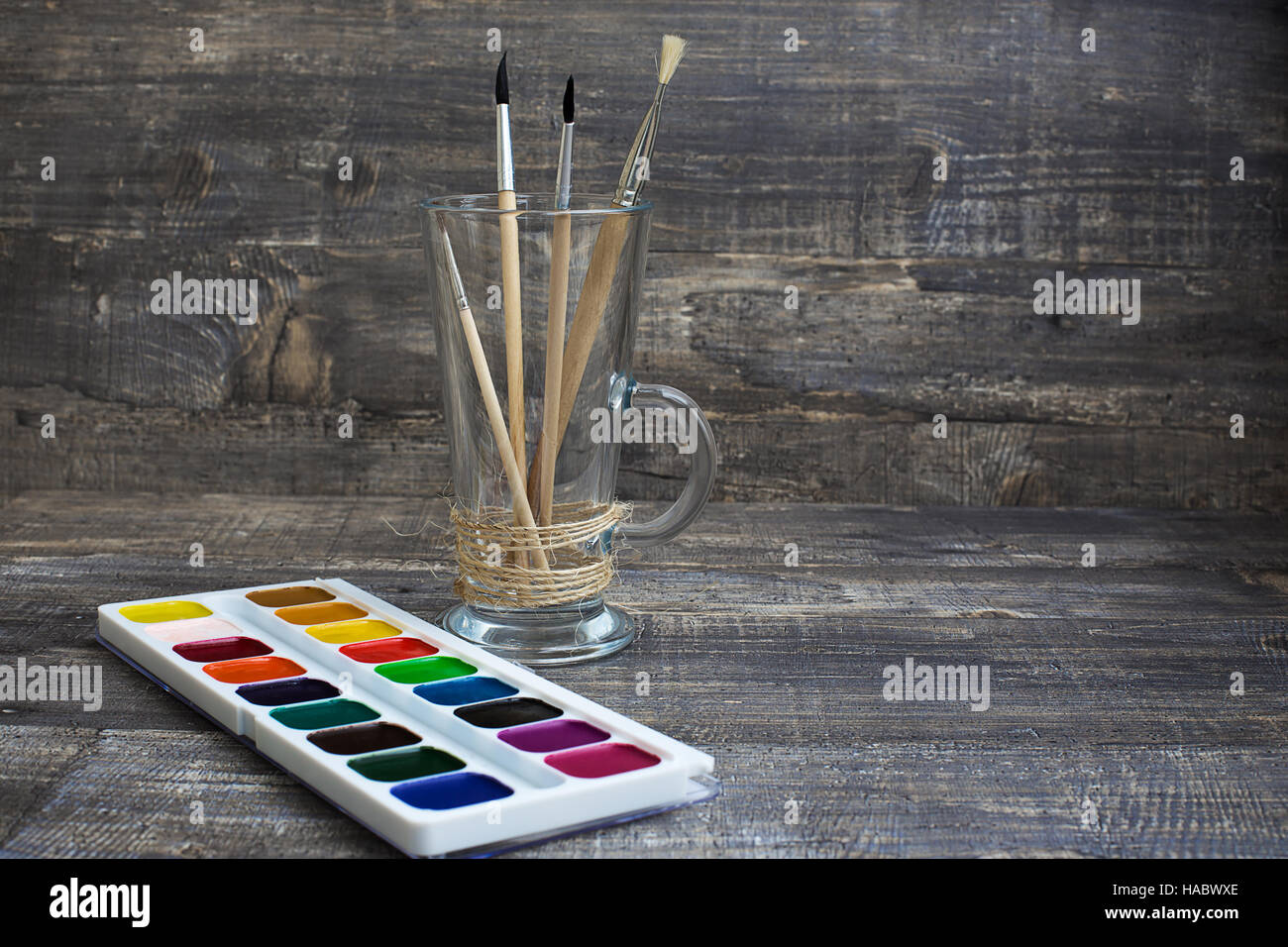 Brushes in vase and watercolor paints on wooden background. Horizontal imagination Stock Photo
