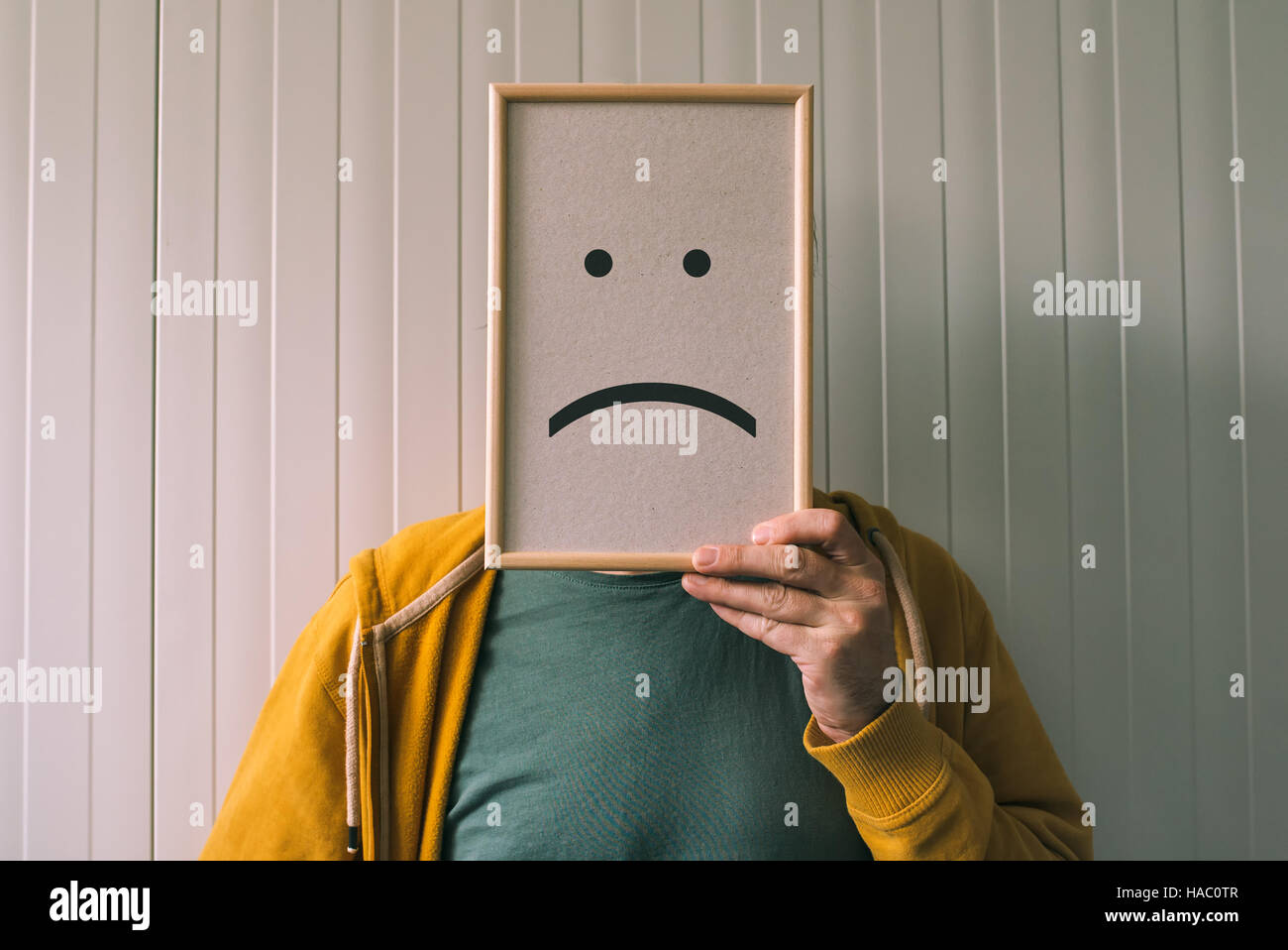 Put a sad pessimistic face on, sadness and depressive emotions concept, man holding picture frame with smiley emoticon printed Stock Photo