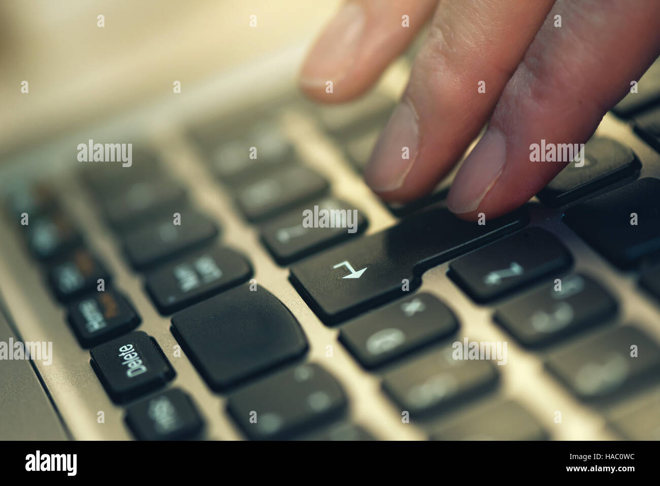 Finger pressing Enter key on laptop computer keyboard, close up, selective focus Stock Photo