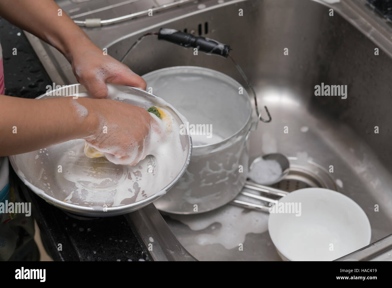kid washing dishware in the kitchen sink with soapy sponge Stock Photo