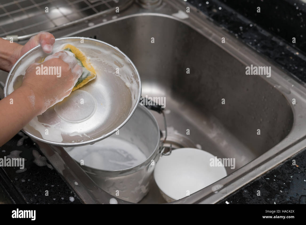 kid washing dishware in the kitchen sink with soapy sponge Stock Photo