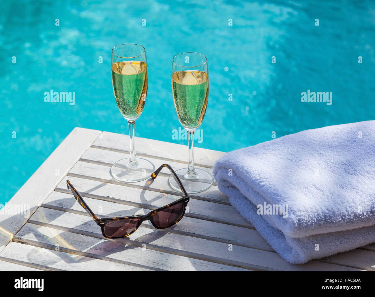 Two glasses of champagne on a white wooden table next to the swimming pool in summer. Stock Photo