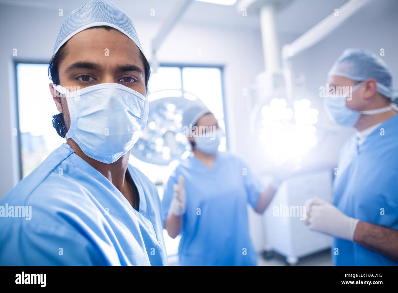 Portrait of male surgeon looking at camera while colleagues interacting ...