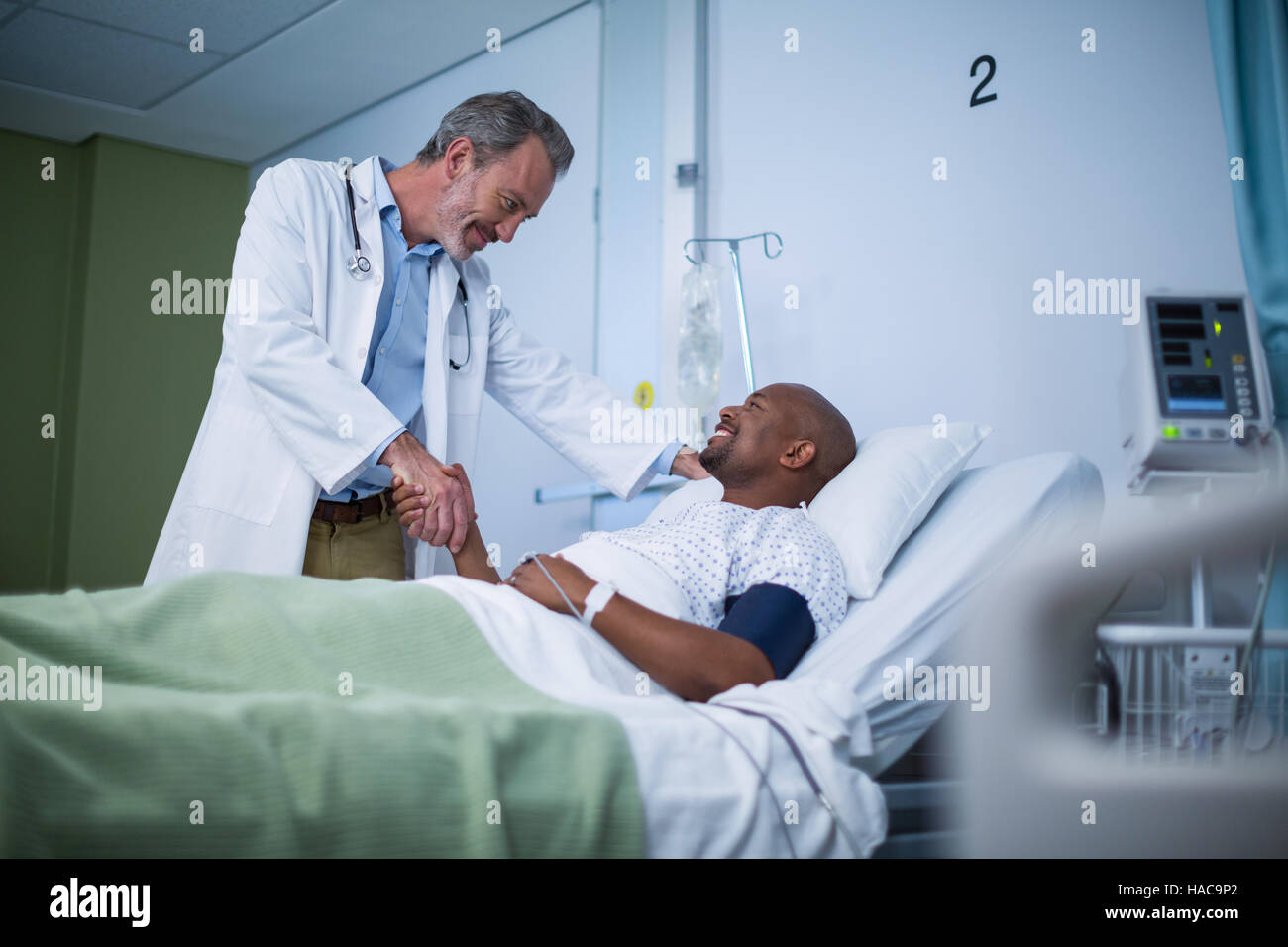 Happy doctor and patient shaking hand in ward Stock Photo