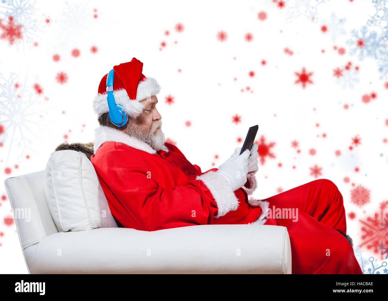 Santa listening to headphones and using digital tablet while sitting on a couch Stock Photo