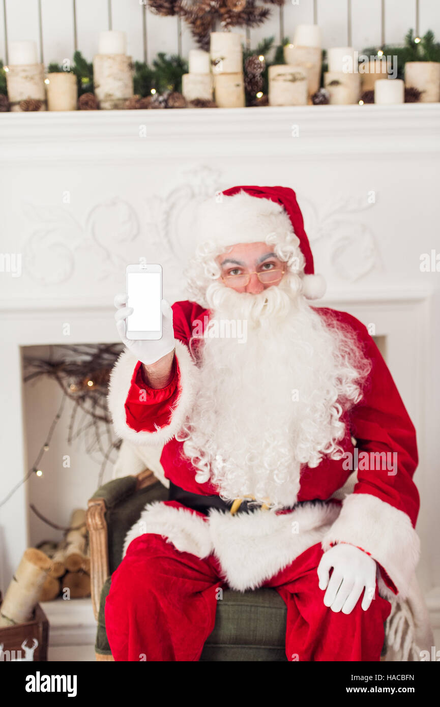 Santa Claus shows a smartphone with fireplace at background Stock Photo ...