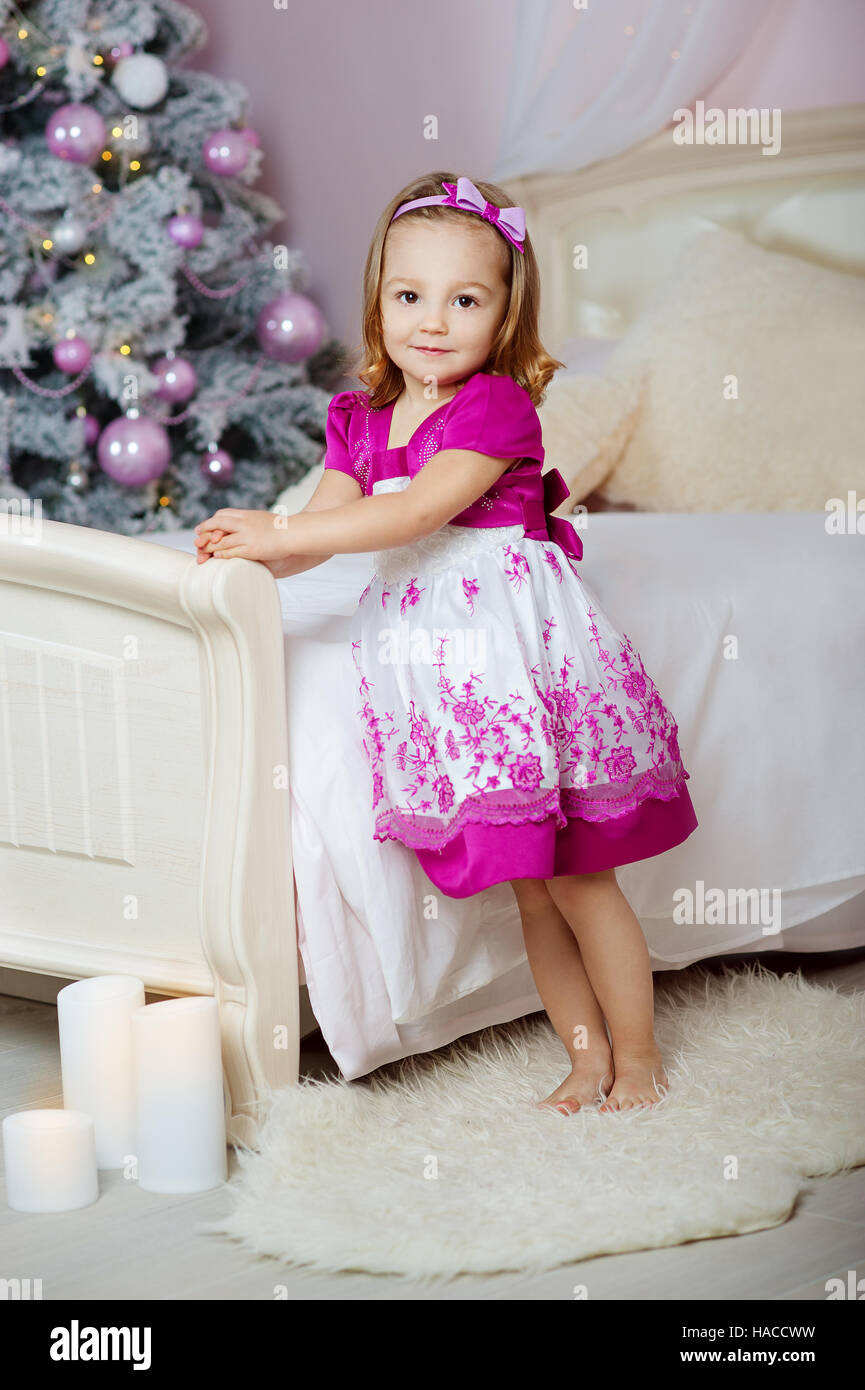 cute little girl in a pink dress standing by the bed on the background ...