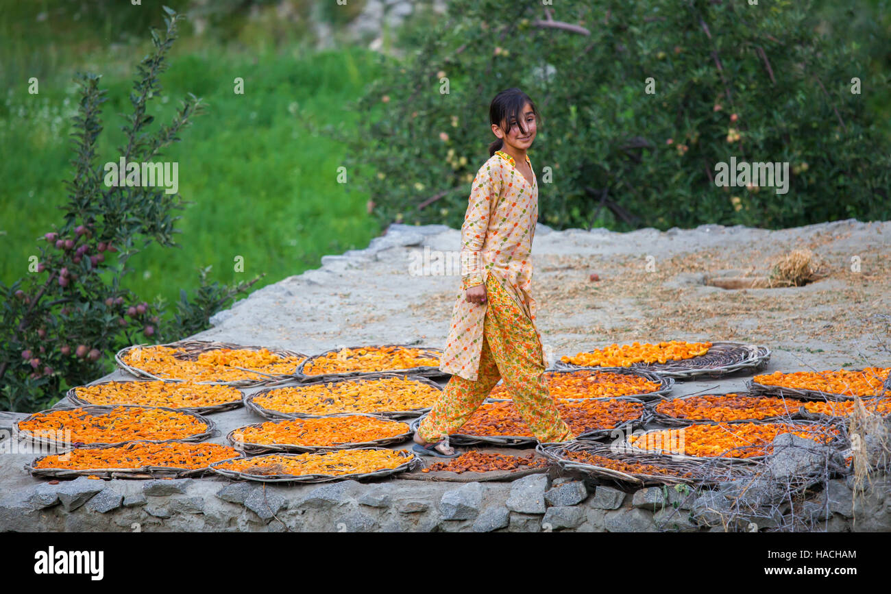 Pakistani girl standing on rooftop drying apricot fruit is smiling