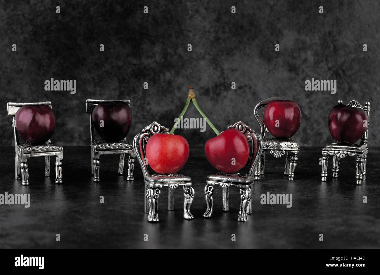 Red delicious ripe cherries on vintage small silver chairs and dark background with copy space Stock Photo