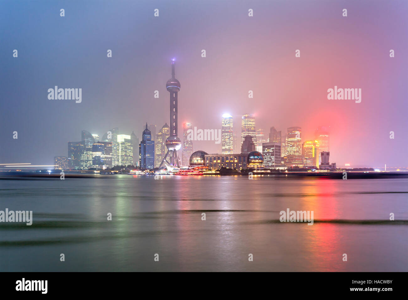 CHina Shanghai Pudong cityscape ofer river at sunset with bright illumination in rainy wet weather. Modern office buildings reflecting in blurred Stock Photo