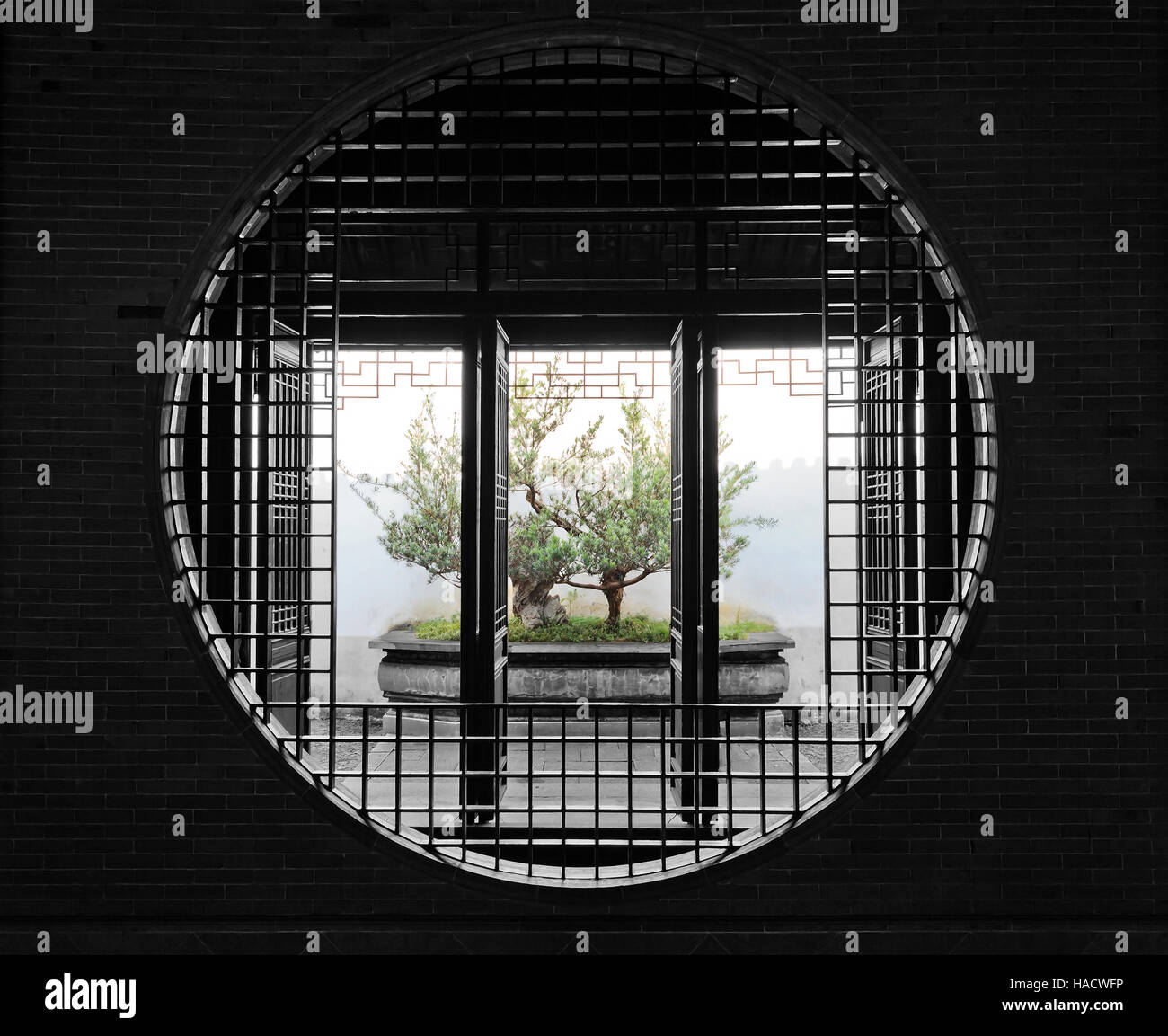 Brick wall and round window door through to open chinese garden and small bonsai tree in a pot. Stock Photo