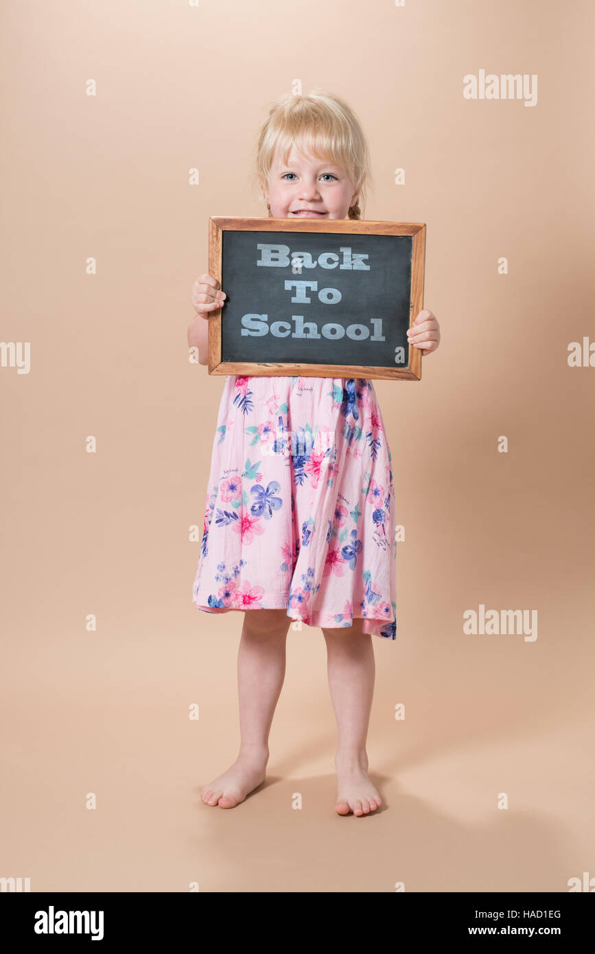 Little girl of school age holding chalk board with 'Back To School' message Stock Photo