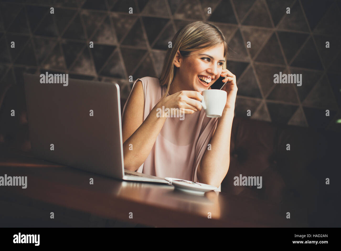 Freelance young woman sitting in the cafeteria with laptop and using  mobile phone Stock Photo