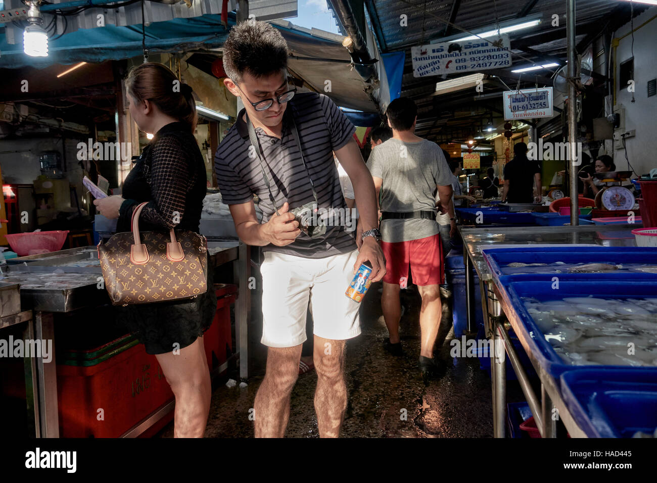 Photographer taking photo.Young man using 'shooting from the hip' technique in attempting to take a photograph in a local market place. Thailand Asia Stock Photo