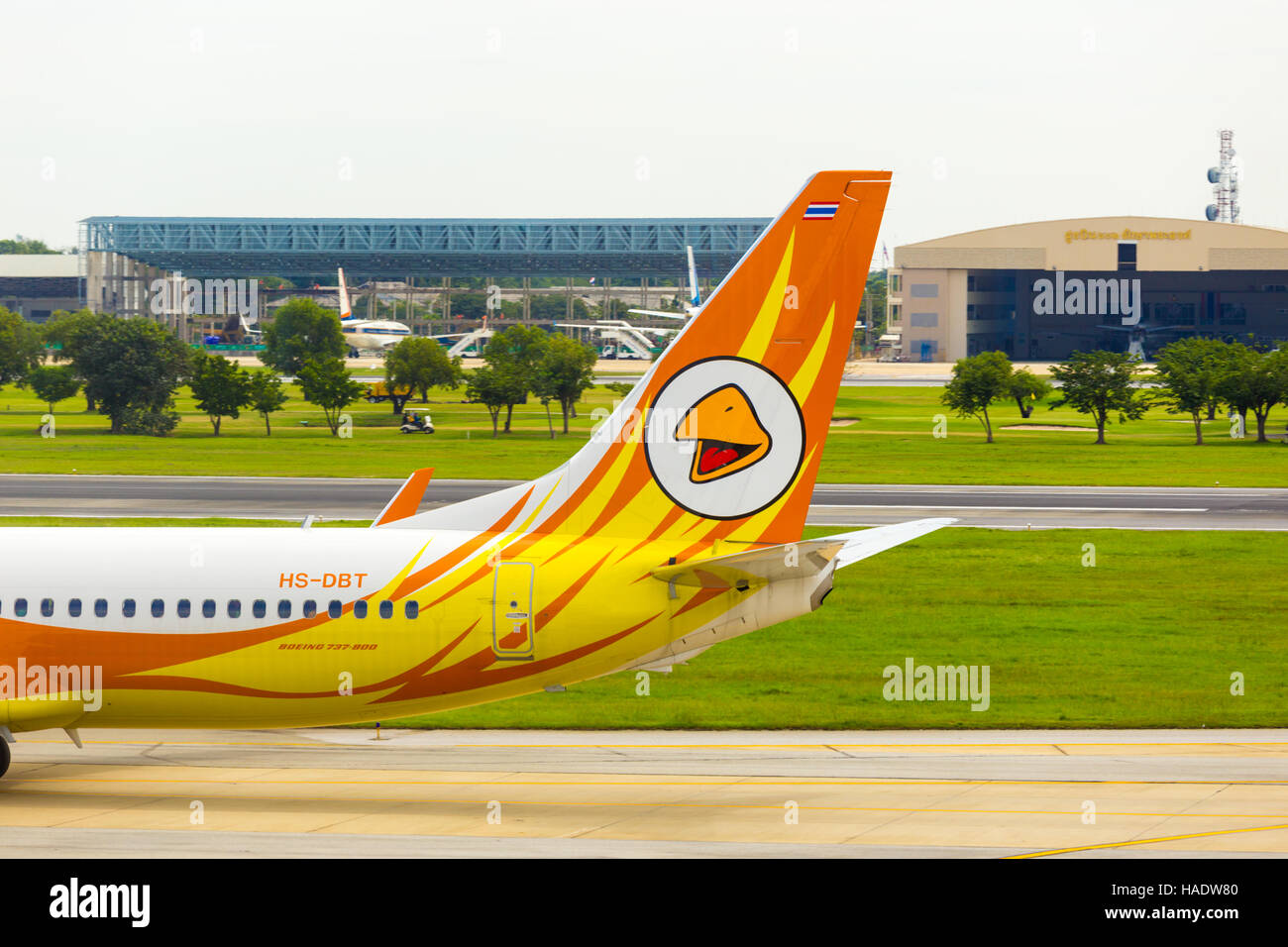 Golf course and golfers in cart visible behind the tail section and logo of low cost carrier, Nok Air airplane taxiing on runway Stock Photo
